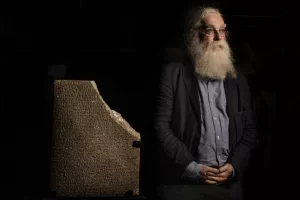 Irving Finkel ao lado de uma tábua com escrita cuneiforme